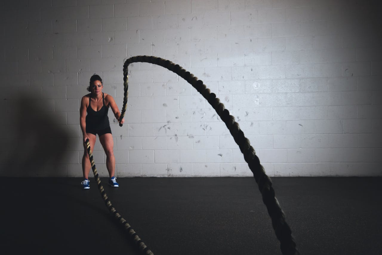 hero-img-01 A focused woman performs a dynamic battle rope exercise in a gym setting, demonstrating strength and fitness.